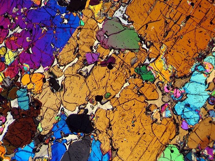 Optical thin section image of NWA 6704 taken in cross-polarized light. Large grains (brown, blue, and black along top) are orthopyroxene; smaller grains (mostly green and purple) are olivine; small opaque (black) grains are chromite and awaruite; and pale gray material between other grains is albite. Width of field is 5 mm. (photo courtesy John Kashuba).